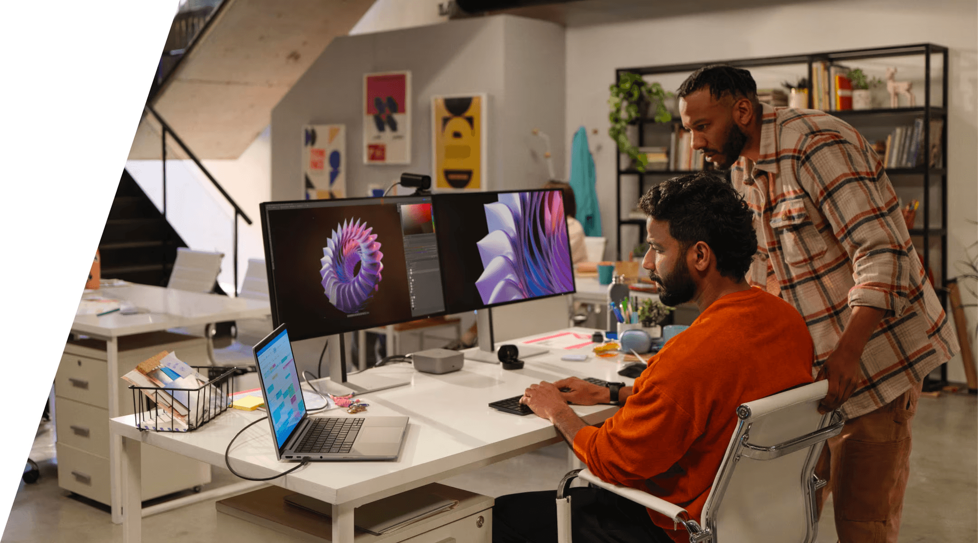 Two professionals collaborating at a modern creative workspace with dual monitors